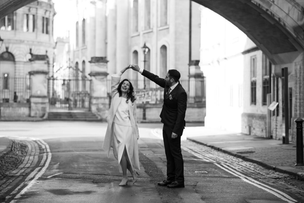 Bride and groom dancing in an empty Oxford street beneath the Bridge of Sighs, black and white photograph