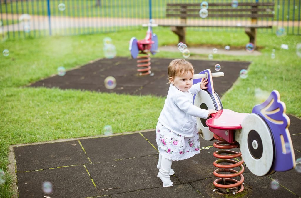 Toddler playing on playground equipment surrounded by floating bubbles