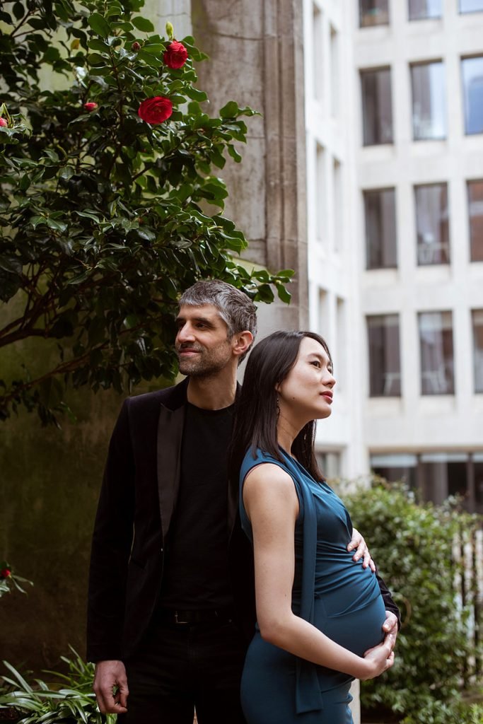 Couple expecting a baby standing together in a London courtyard garden with roses