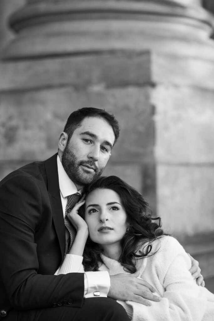 Close portrait of a couple leaning together against a stone column, black and white photograph
