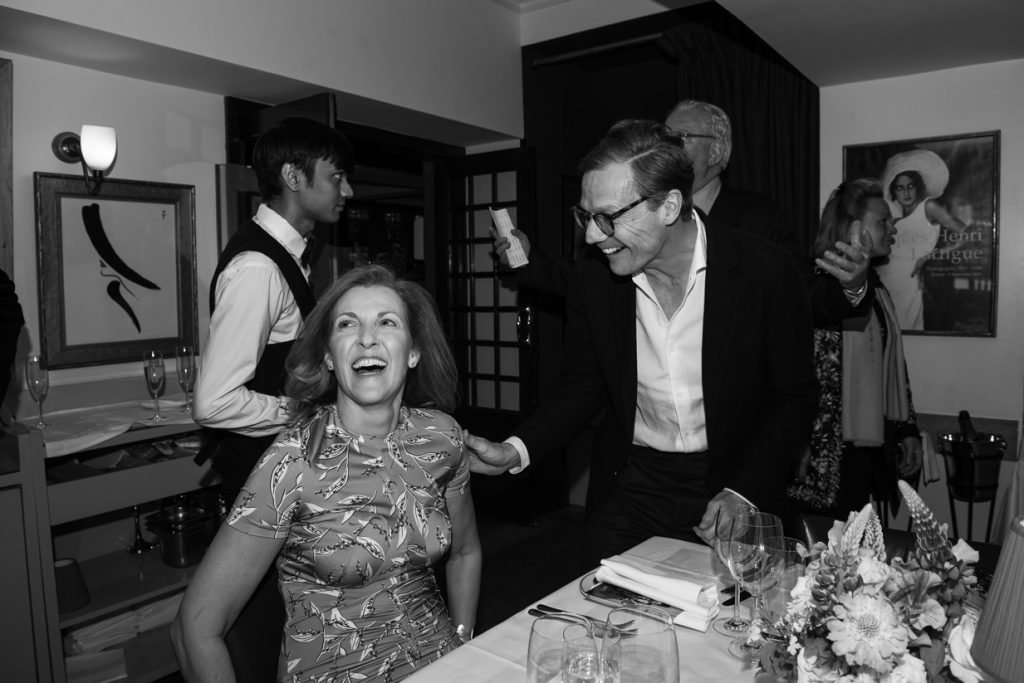 Guests laughing at a dinner table, black and white photograph