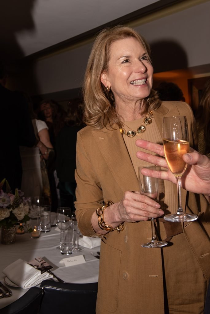 Guest in a tan jacket laughing as glasses are handed round at a dinner