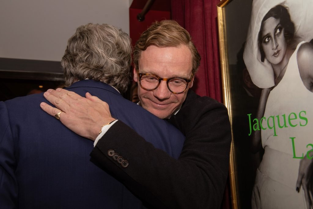 Two guests embracing beside a framed poster at a private view