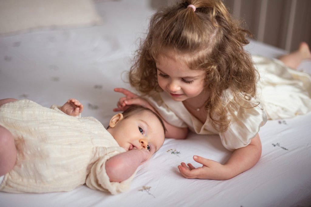 Young girl leaning over her newborn sibling on a bed