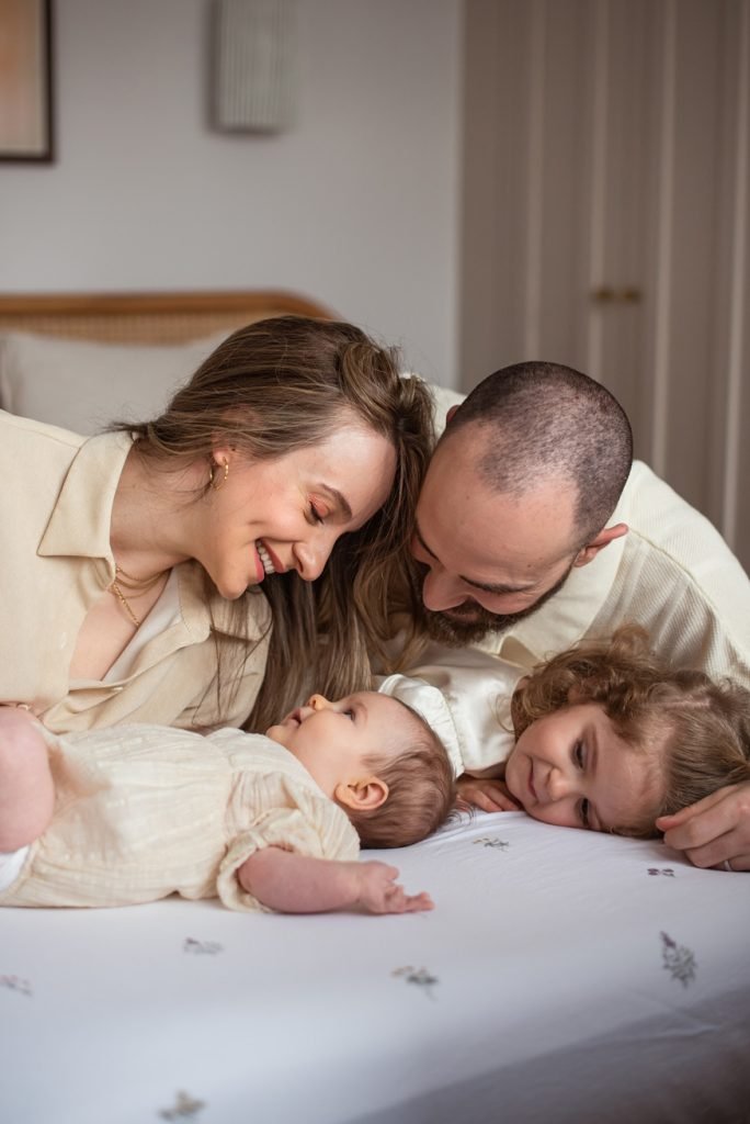 Parents and their small daughter lying on a bed beside the new baby