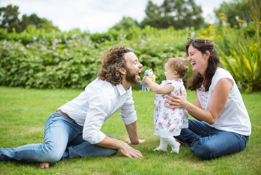 Parents kneeling on the grass on either side of their toddler