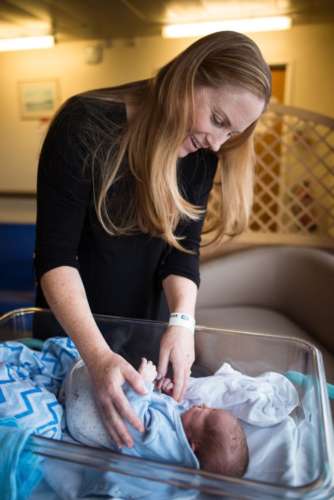 Mother reaching into a hospital crib to touch her newborn