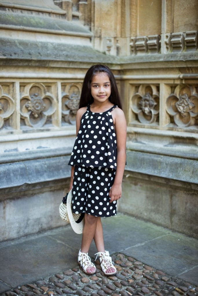 Girl in a polka-dot dress standing against carved stonework