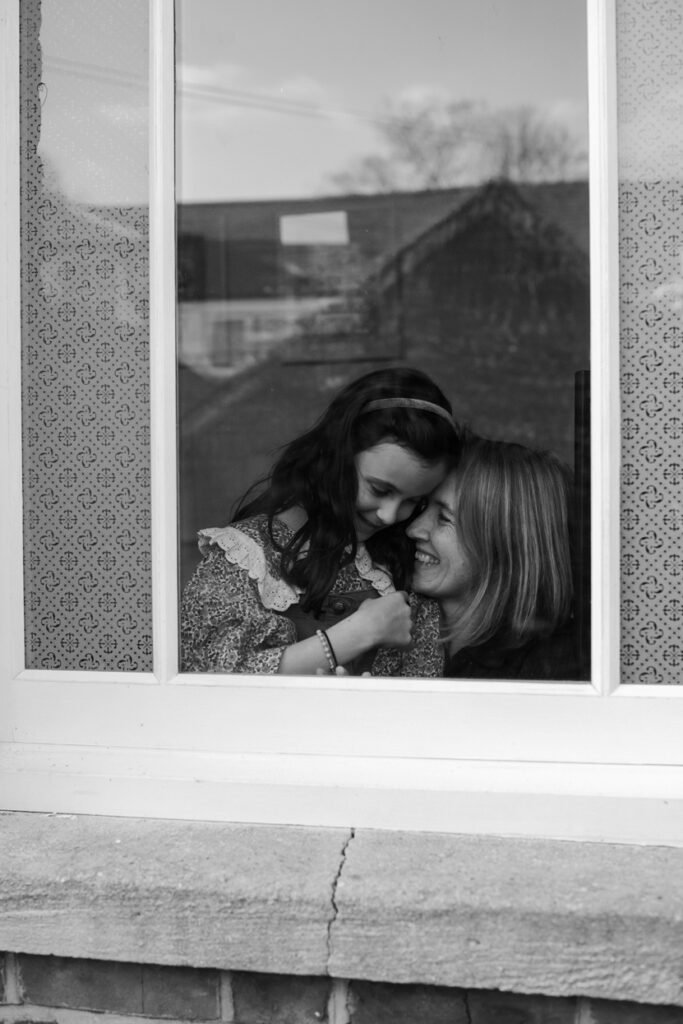 Two sisters laughing together, seen through a window with the street reflected in the glass