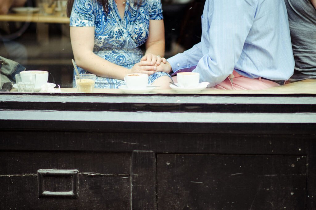 Couple holding hands across a café table, seen through the window