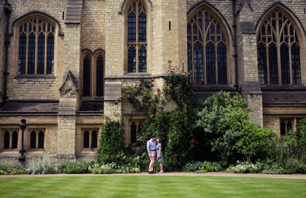 Couple standing small against the front of a Gothic college building