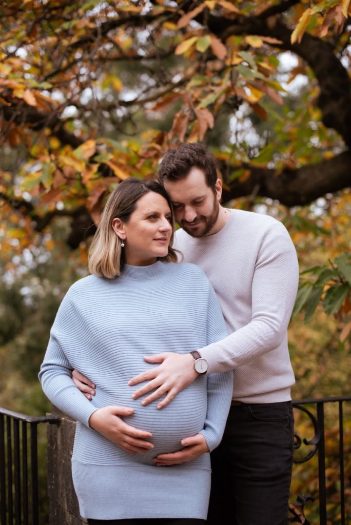 Expectant couple holding her bump together under an autumn tree