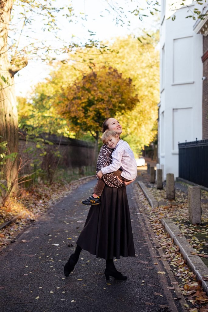 Mother carrying her small daughter down a leafy autumn lane