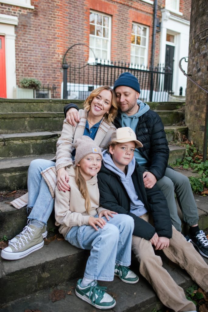 Family of five sitting on the front steps of a brick London house