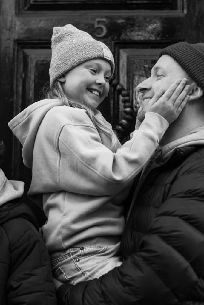 Girl in a woolly hat holding her father's face in her hands, black and white photograph