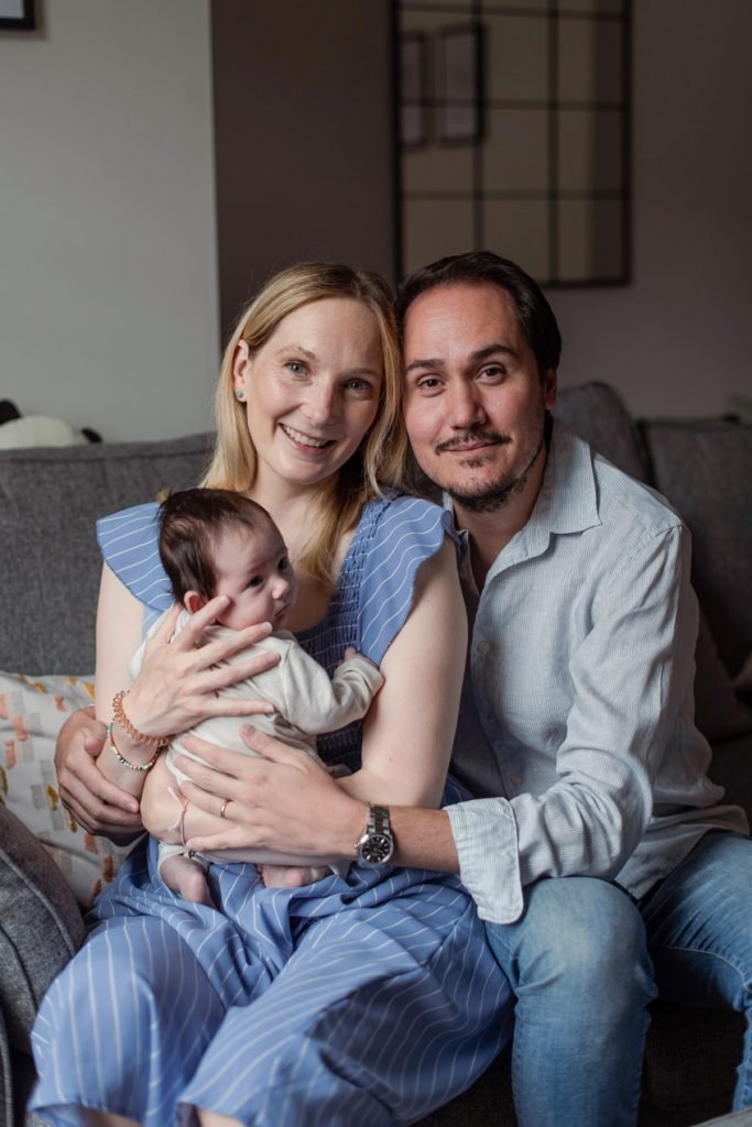 Parents sitting together on a sofa with their newborn between them