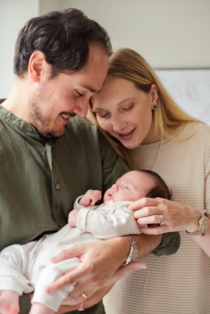 Parents holding their newborn between them, foreheads touching
