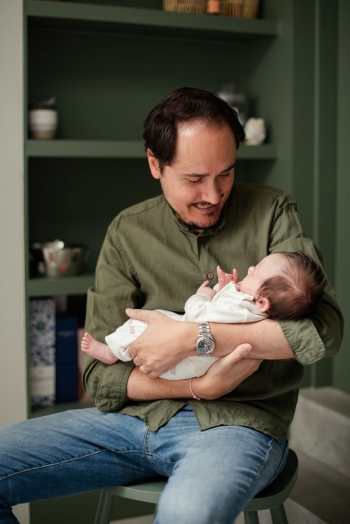 Father holding his newborn in a green-panelled kitchen