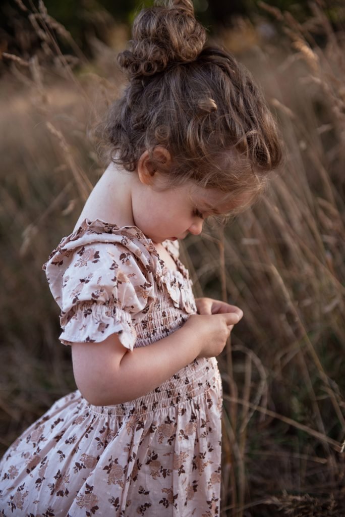 Small girl in a floral dress looking down amid tall summer grass