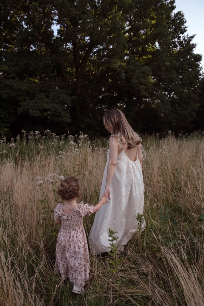 Mother and small daughter walking hand in hand through a meadow at dusk