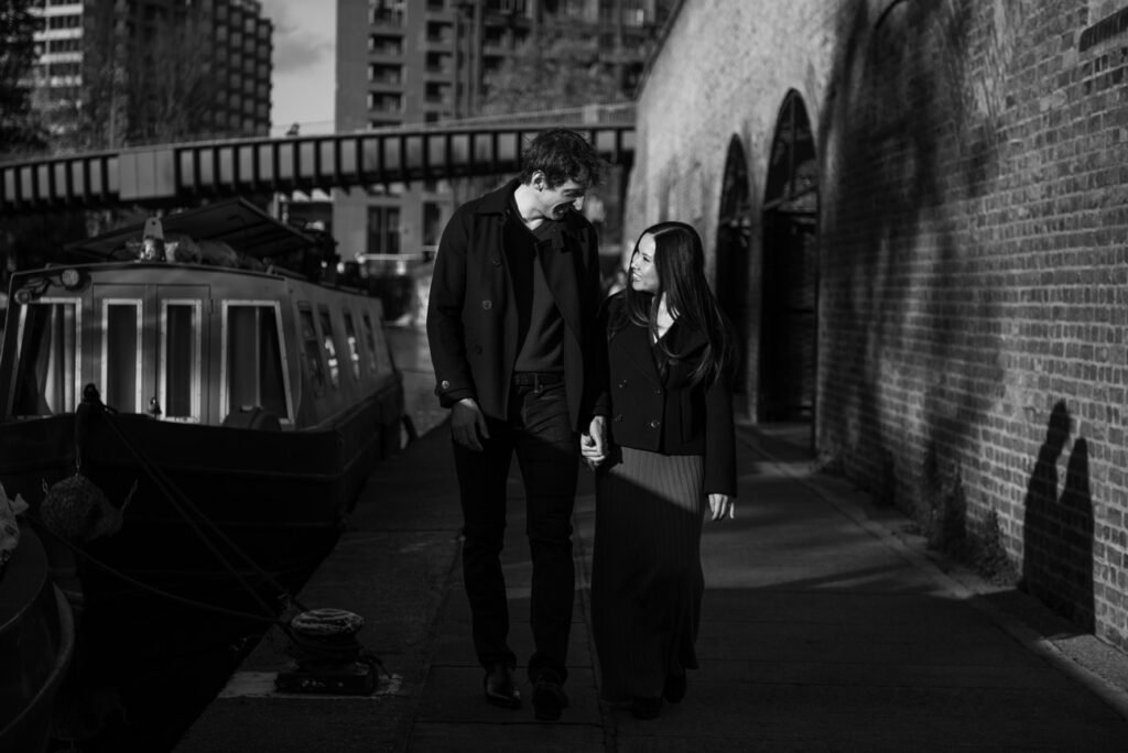 Couple walking a canal towpath past a moored narrowboat, black and white photograph