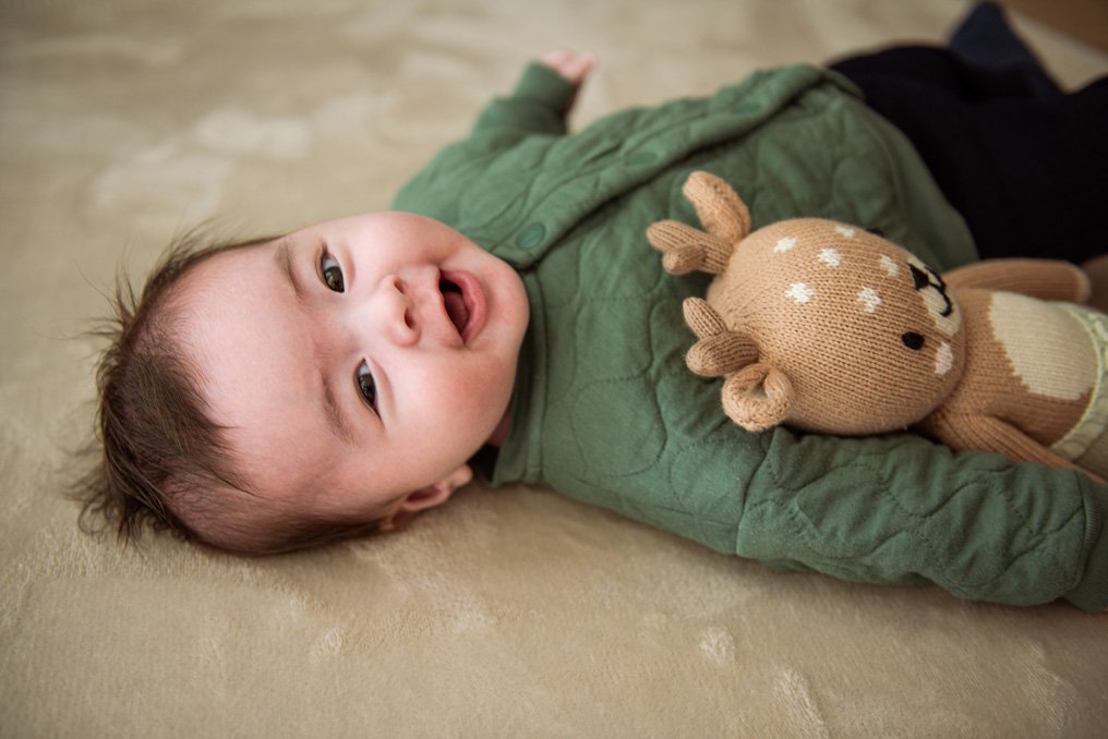 Baby lying on a blanket beside a knitted deer toy