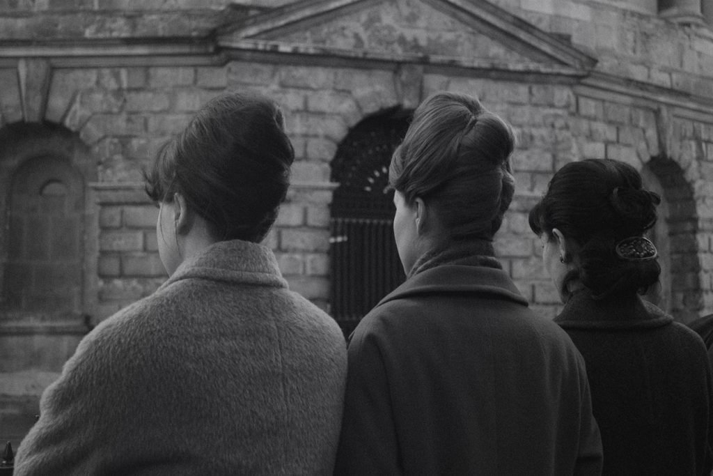 Three people seen from behind watching a ceremony, black and white photograph