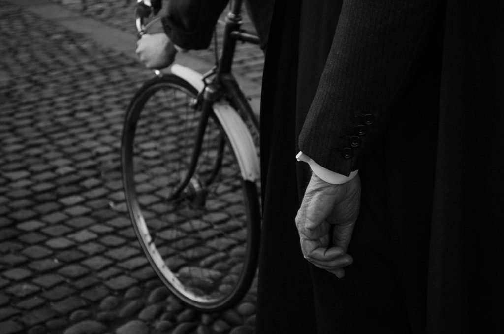 Cyclist passing a figure in a dark coat on cobbles, black and white photograph