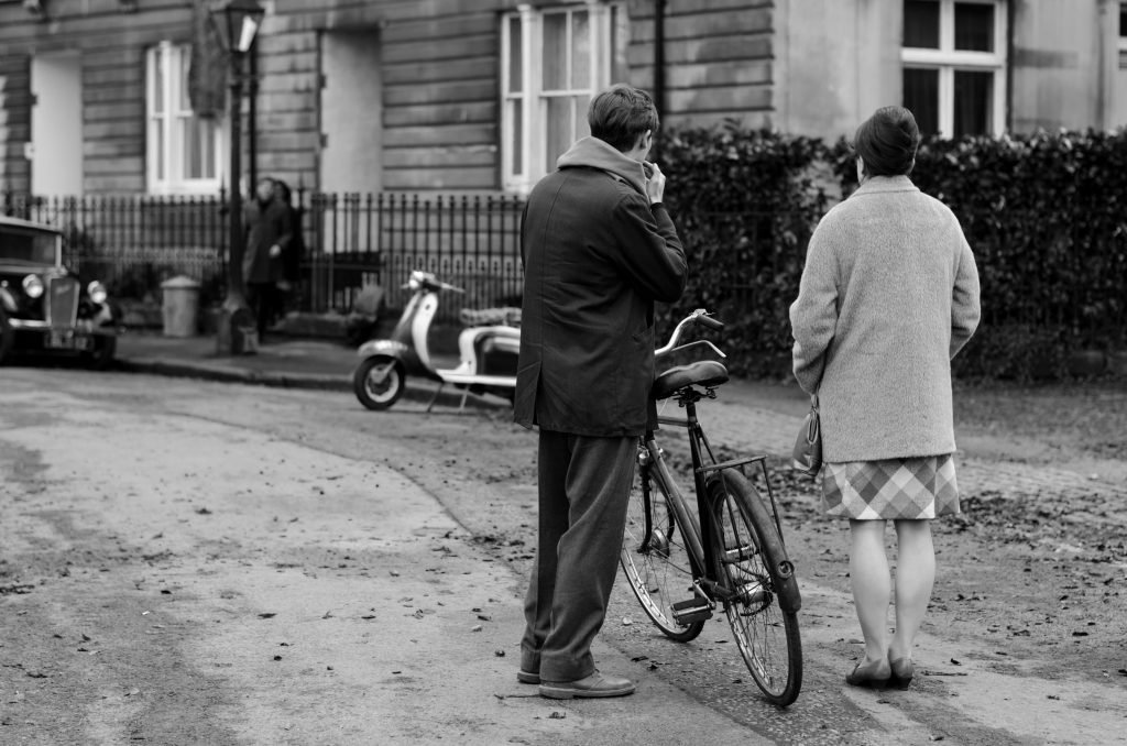 Man with a bicycle and a woman crossing a street, black and white photograph