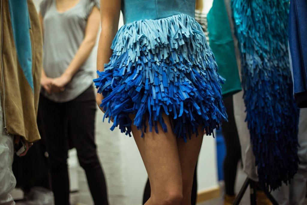 Models in blue fringed dresses waiting backstage