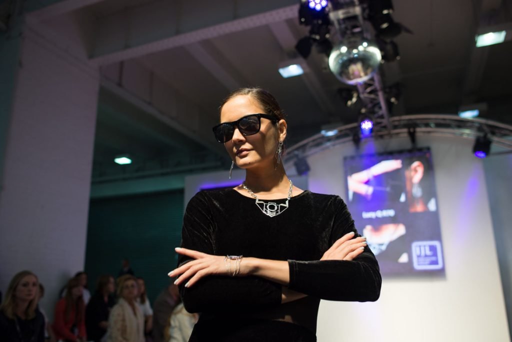 Presenter in sunglasses standing under stage lights, arms folded