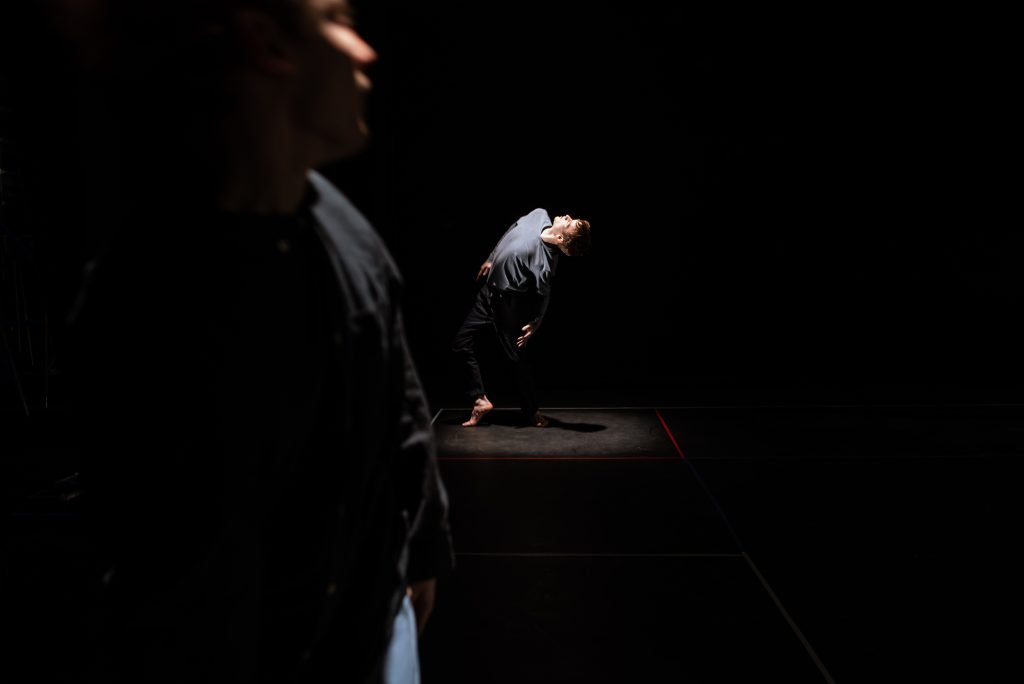 Dancer bending backwards in a pool of light on a dark stage
