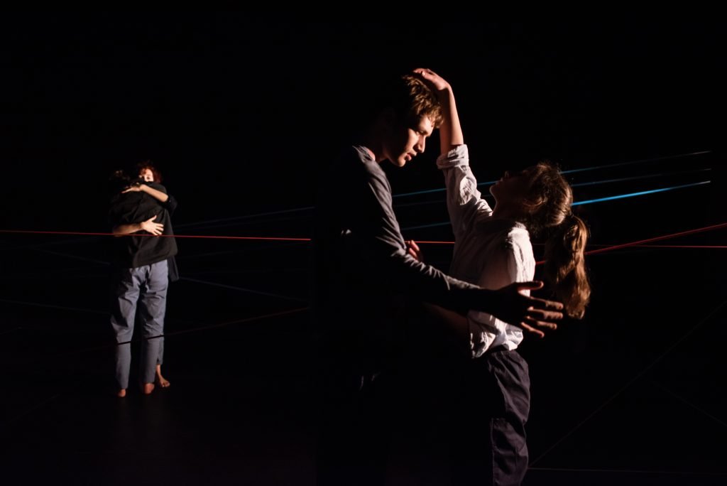 Two pairs of dancers lifting and turning under coloured beams
