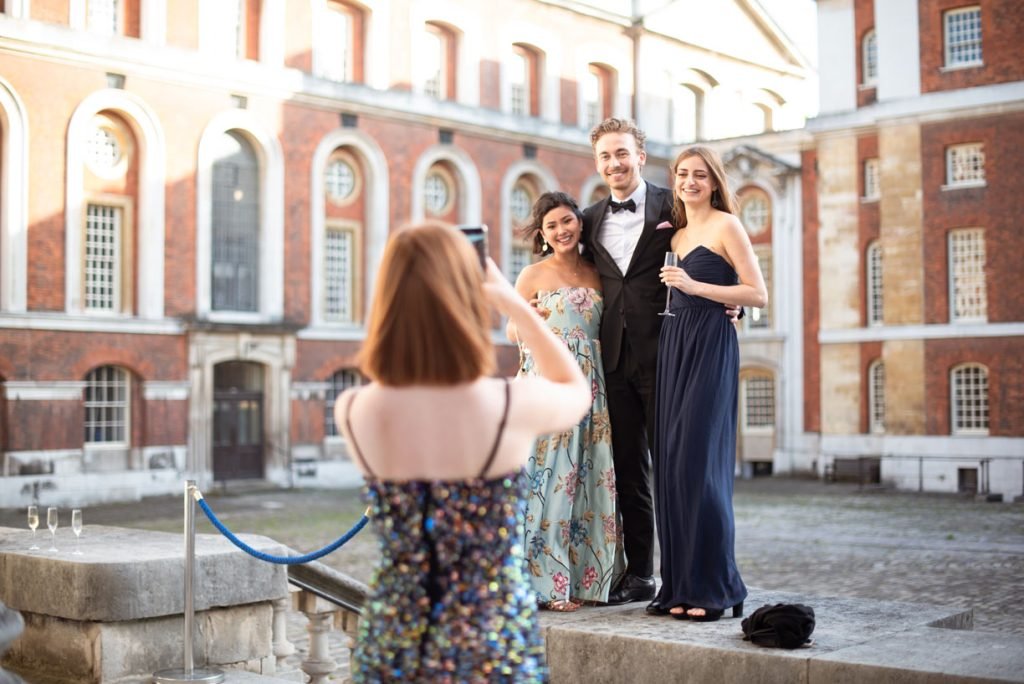 Guest photographing three friends in evening dress in a courtyard