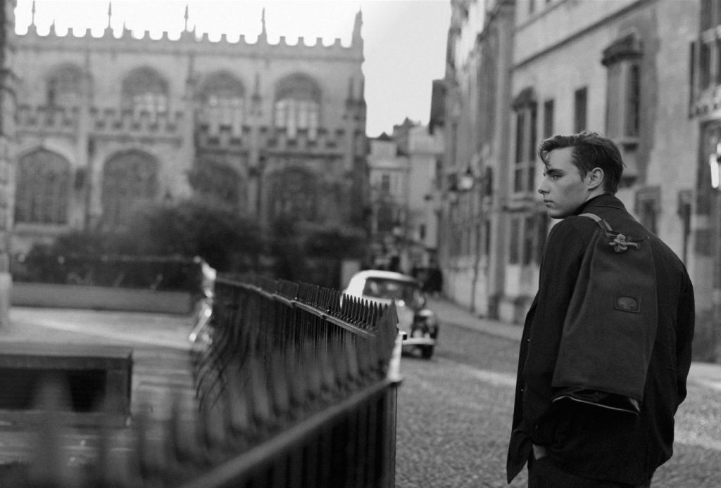 Man with a rucksack walking past college railings, black and white photograph