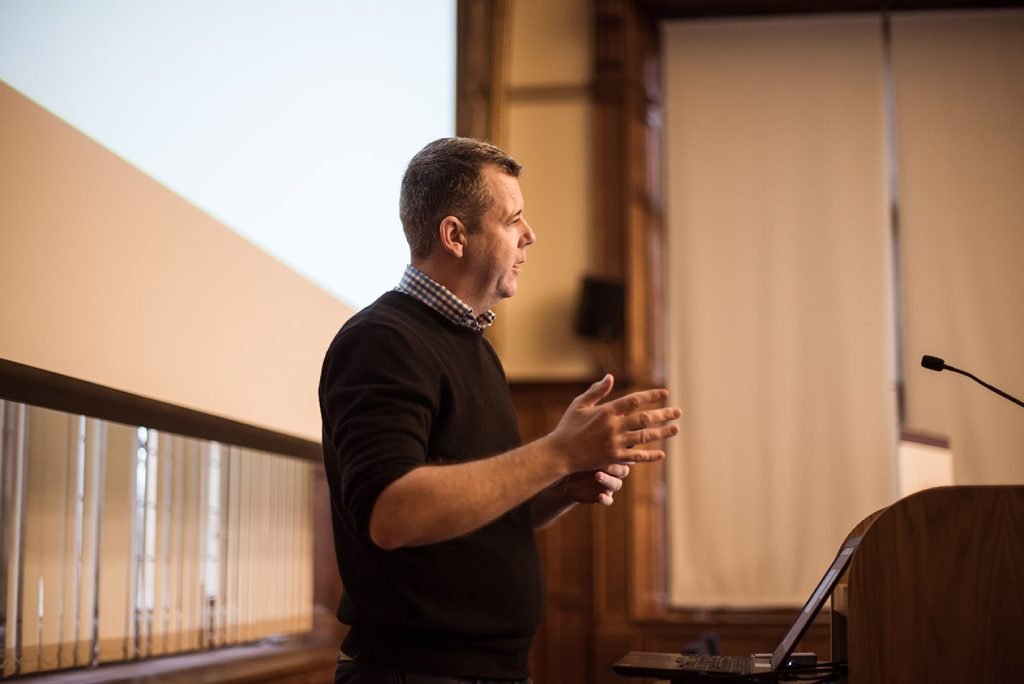 Speaker addressing a room, gesturing mid-sentence