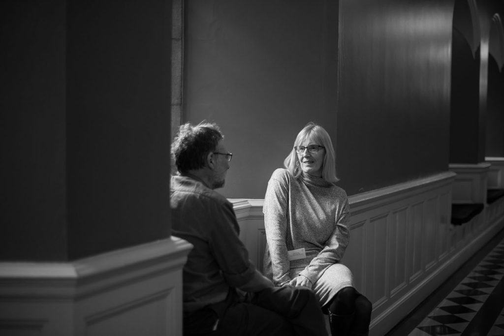 Two people talking in a panelled hall, black and white photograph