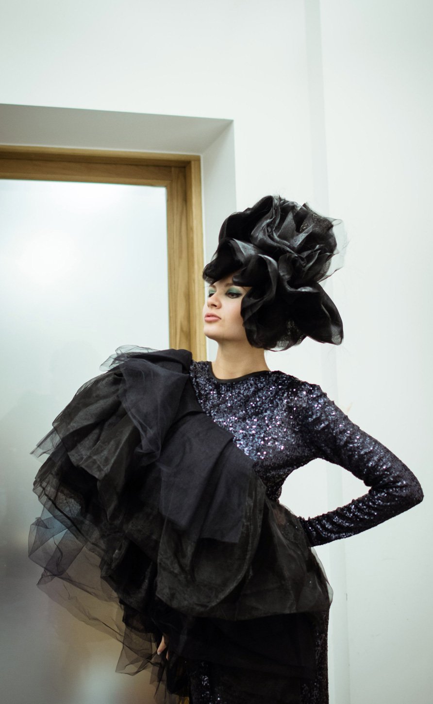 Model in a black feathered hat and ruffled dress in a doorway