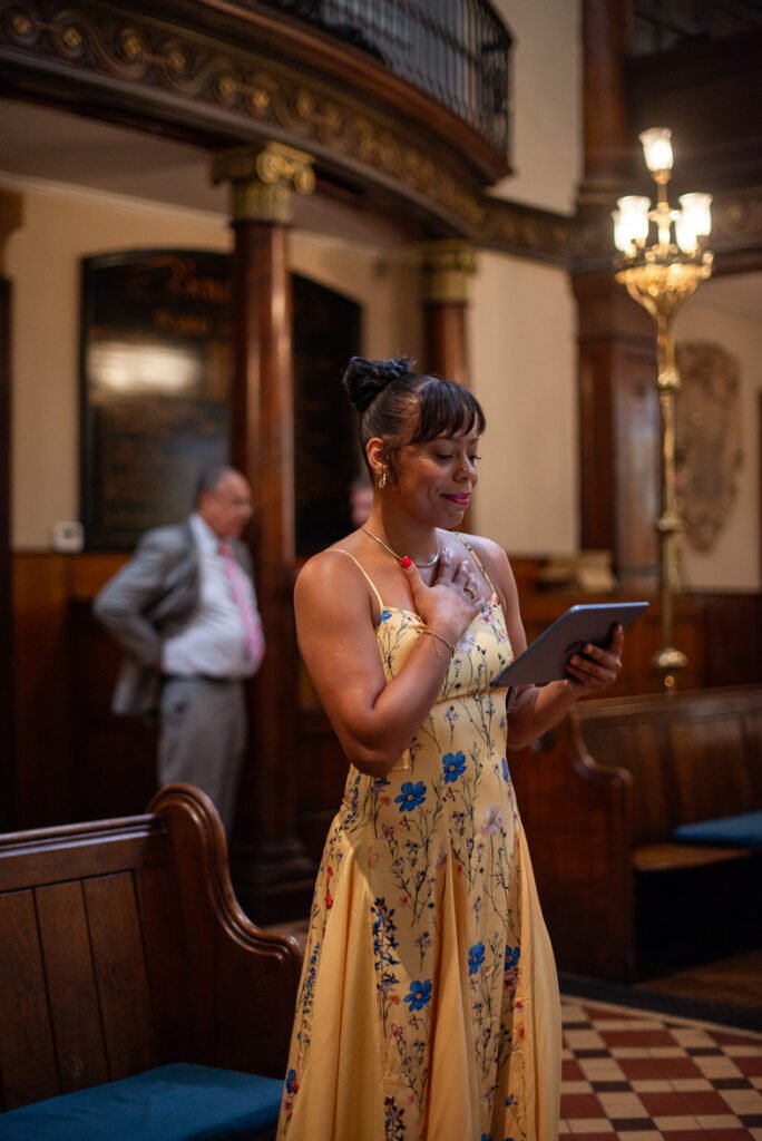 Guest in a yellow floral dress giving a reading at a wedding ceremony