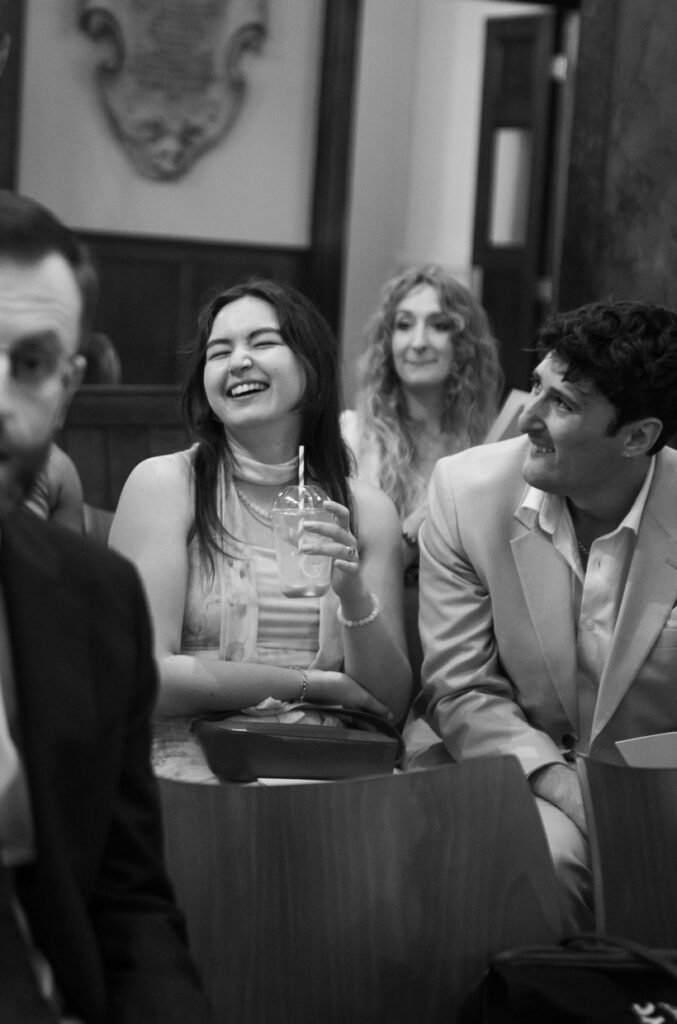 Guests laughing together over drinks at a wedding reception, black and white photograph