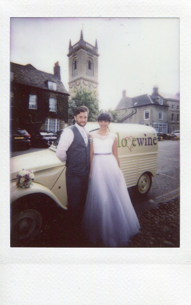 Instant photograph of a bride and groom beside a wine van outside a village church