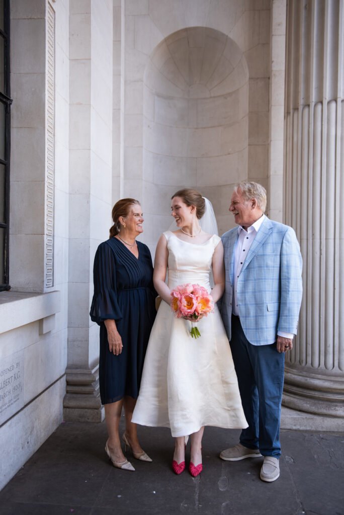 Bride with her parents between the stone columns of Old Marylebone Town Hall
