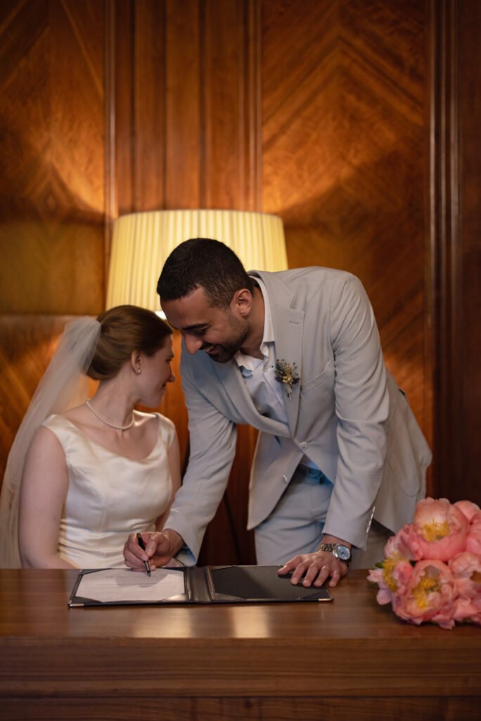 Bride signing the register while her groom leans in beside her