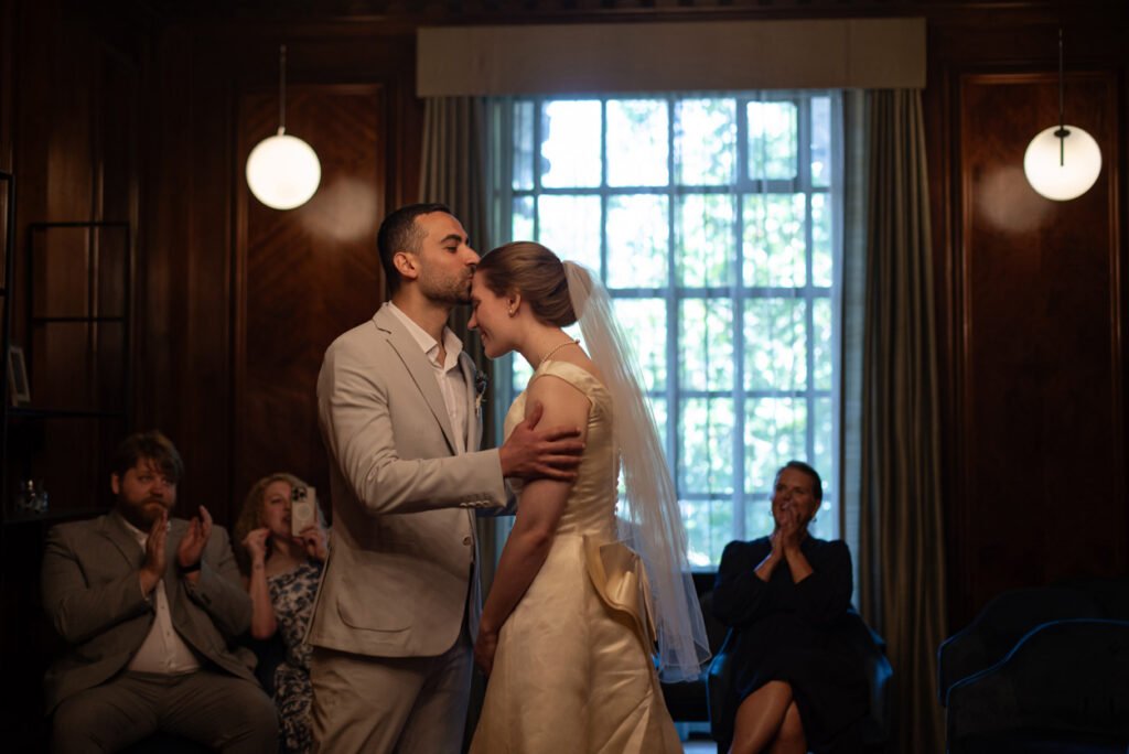 Bride and groom kissing at the front of the ceremony room as guests applaud
