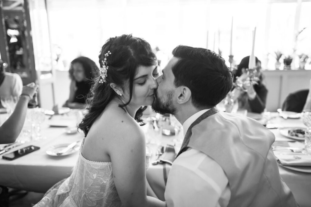 Bride and groom kissing at the wedding breakfast table, black and white photograph
