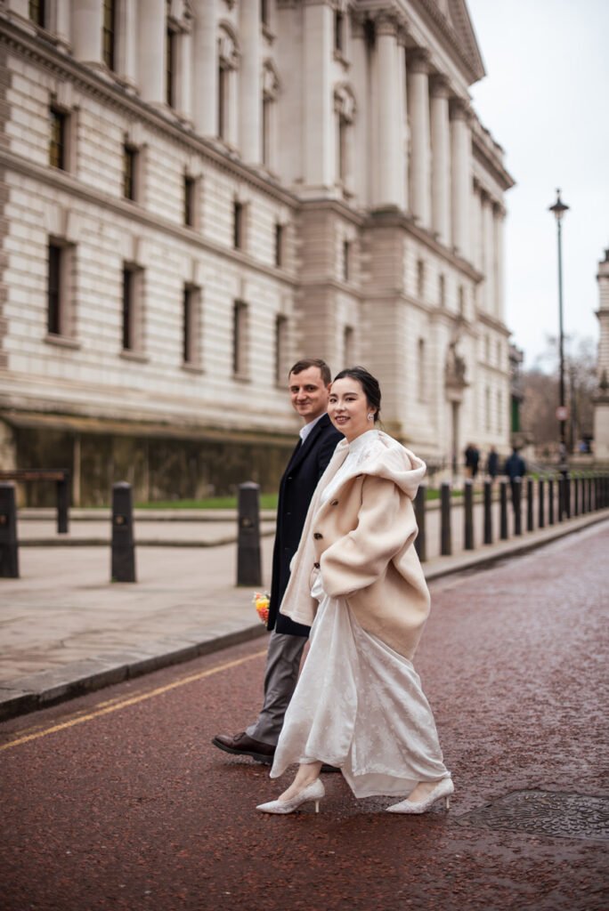 Bride in a cream coat walking a London street arm in arm with her groom