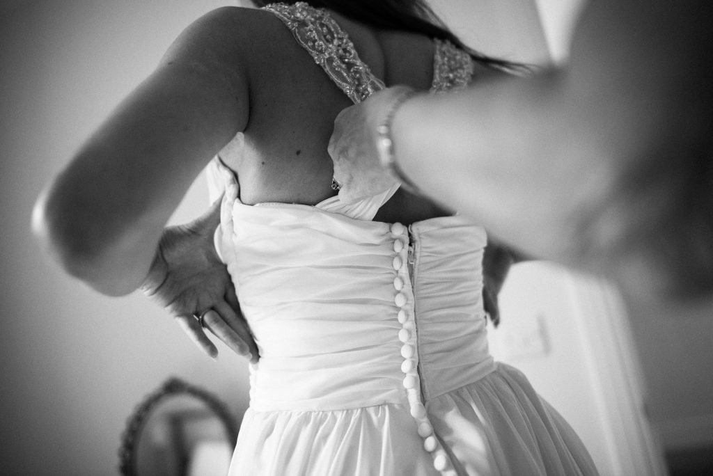 Bridesmaid buttoning the back of the bride's dress, black and white photograph