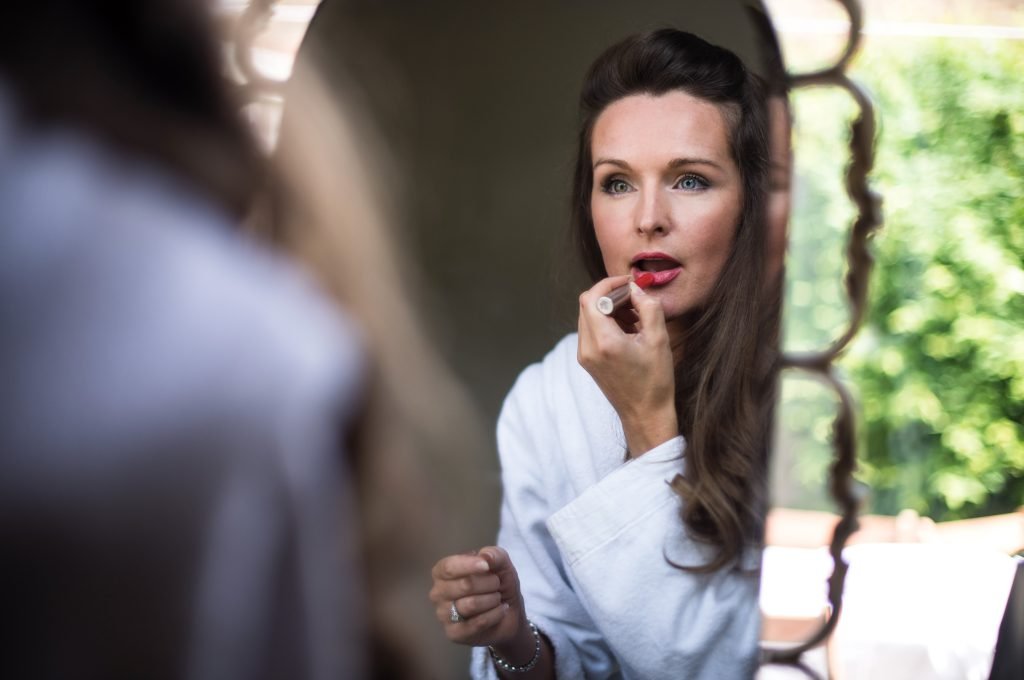 Bride putting on lipstick at a mirror before the ceremony