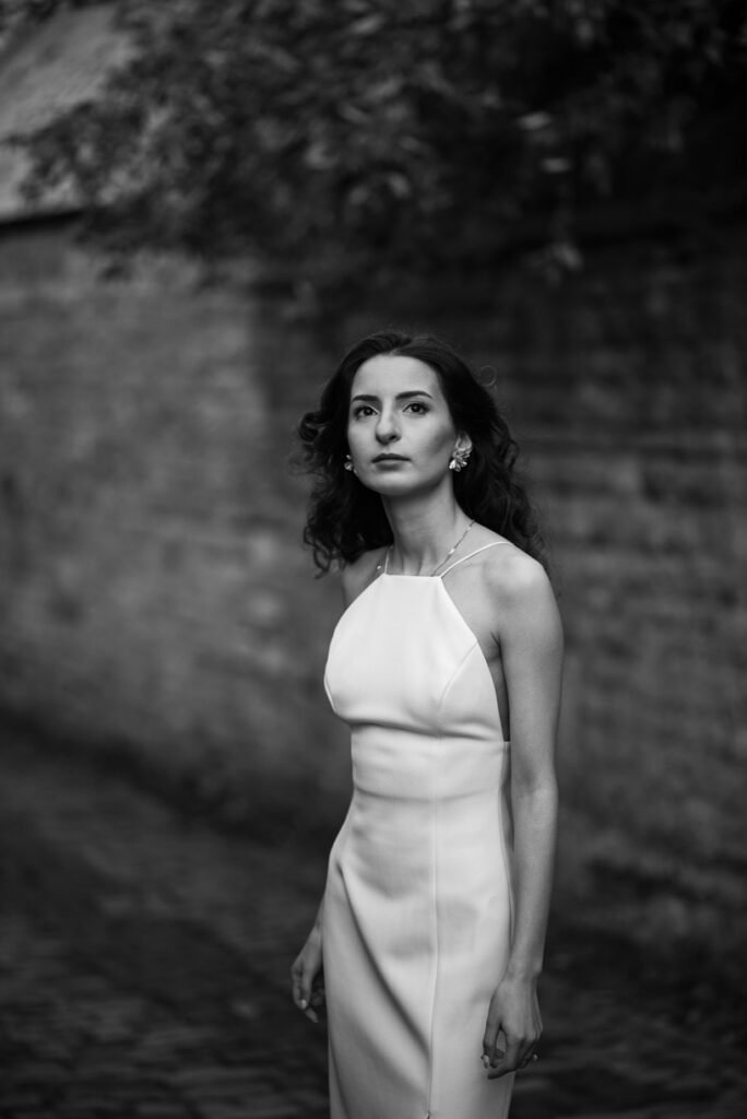 Bride in a white halter-neck dress standing against a flint wall, black and white photograph