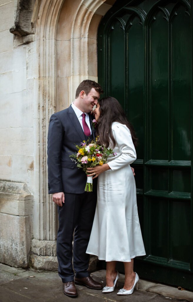 Bride and groom touching foreheads in an arched church doorway, wildflower bouquet in hand